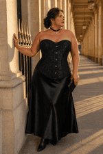 Corset noir fleuri grande taille en jacquard ton sur ton, avec fermeture à busc métallique sur le devant et coupe cintrée mettant en valeur la silhouette. Présenté dans un look élégant avec une jupe longue en satin noir lors d'une séance photo éditoriale a la galerie de montpensier a Paris.