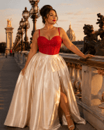 Corset soutien-gorge rouge à strass porté avec une longue jupe satinée crème sur le Pont Alexandre III à Paris au coucher du soleil.