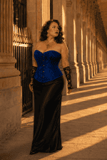 Corset vénitien bleu royal grande taille en jacquard satiné à motif floral ton sur ton, avec fermeture à busc métallique sur le devant, porté avec une jupe longue noire élégante a la galerie de montpensier a Paris au coucher du soleil.