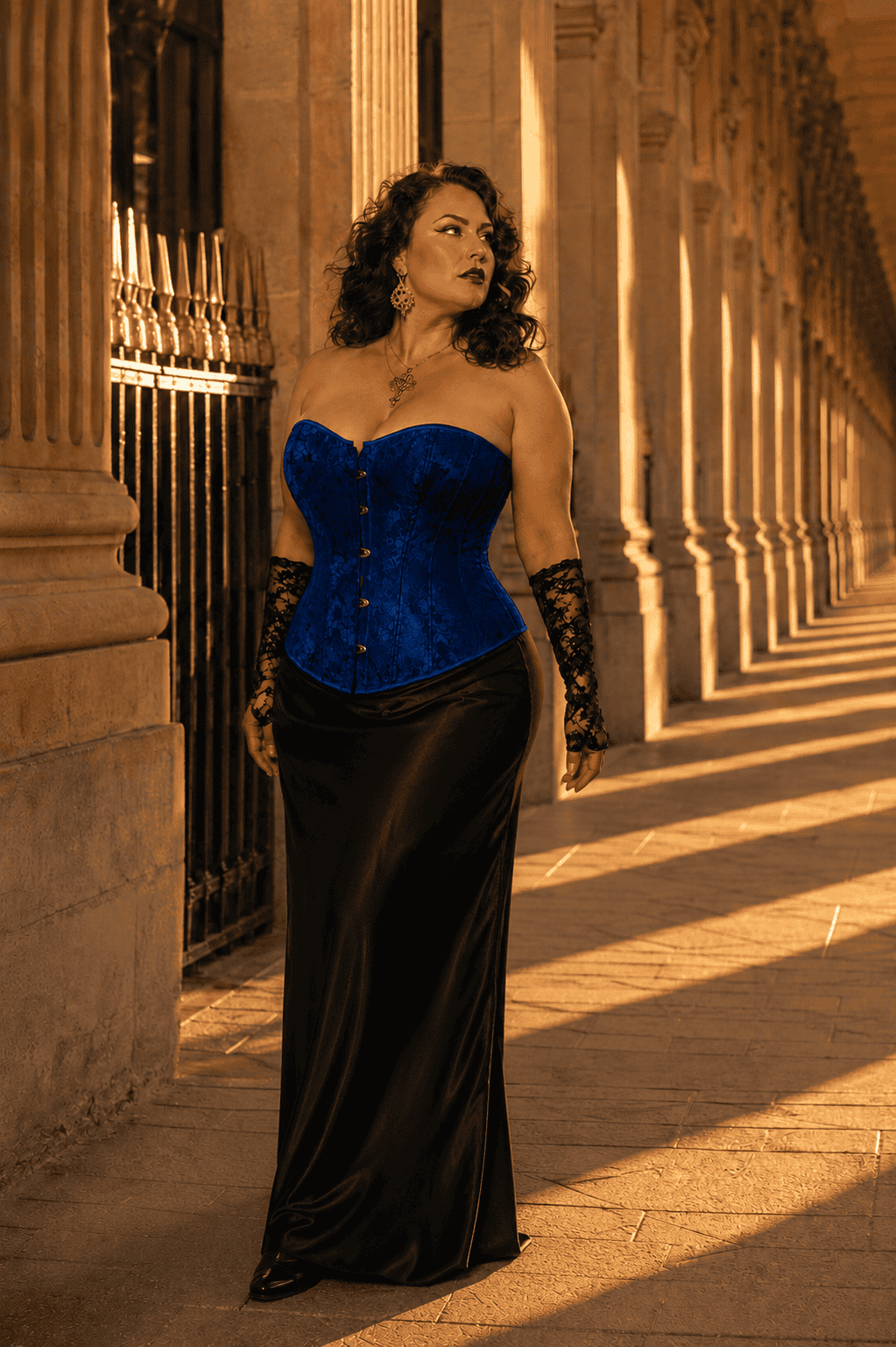 Corset vénitien bleu royal grande taille en jacquard satiné à motif floral ton sur ton, avec fermeture à busc métallique sur le devant, porté avec une jupe longue noire élégante a la galerie de montpensier a Paris au coucher du soleil.