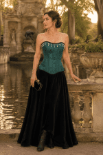 Photo éditoriale de mode d'un corset victorien moderne vert sarcelle en jacquard à motif floral ton sur ton, orné d'une frange de perles blanches, porté avec une longue jupe noire en velours à la Fontaine de Médicis à Paris.
