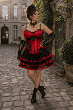 Femme de 45 ans portant une robe corset bustier gothique noire et rouge à jupe courte à volants dans la cour du musée Carnavalet à Paris.